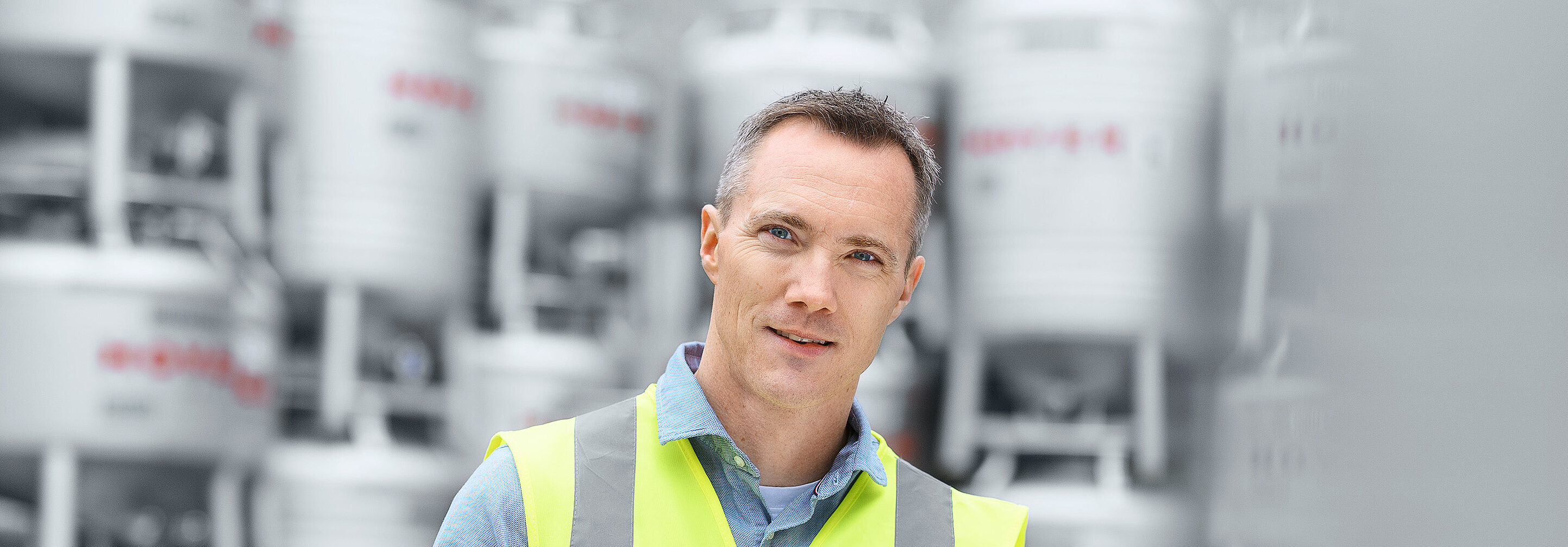 员工穿着安全背心，手持平板，站在堆放在室外的 HOYER IBC 容器前