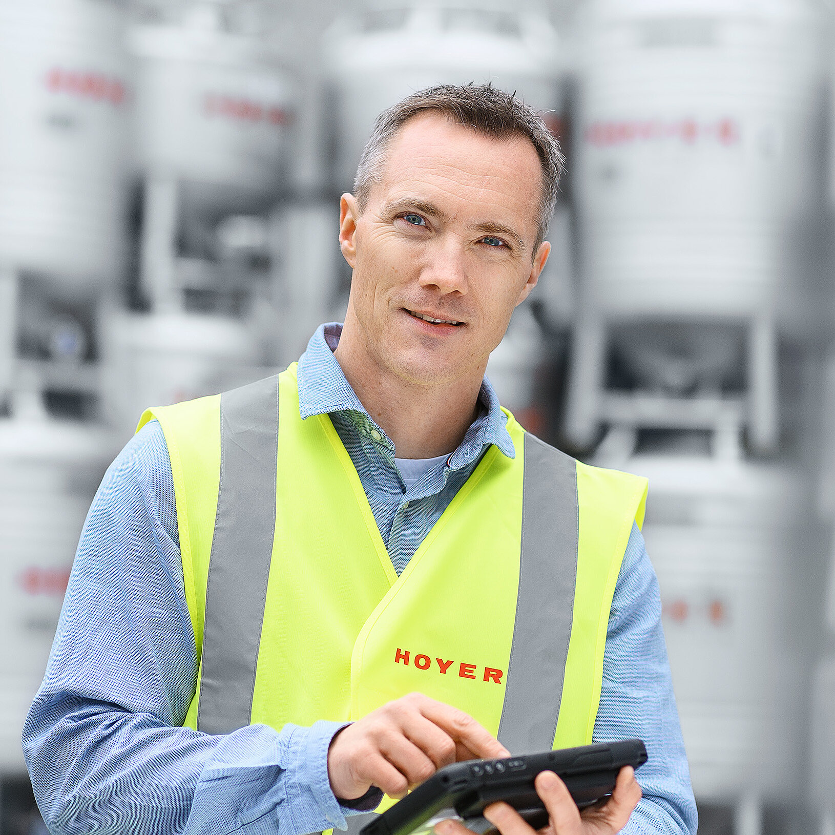 员工穿着安全背心，手持平板，站在堆放在室外的 HOYER IBC 容器前
