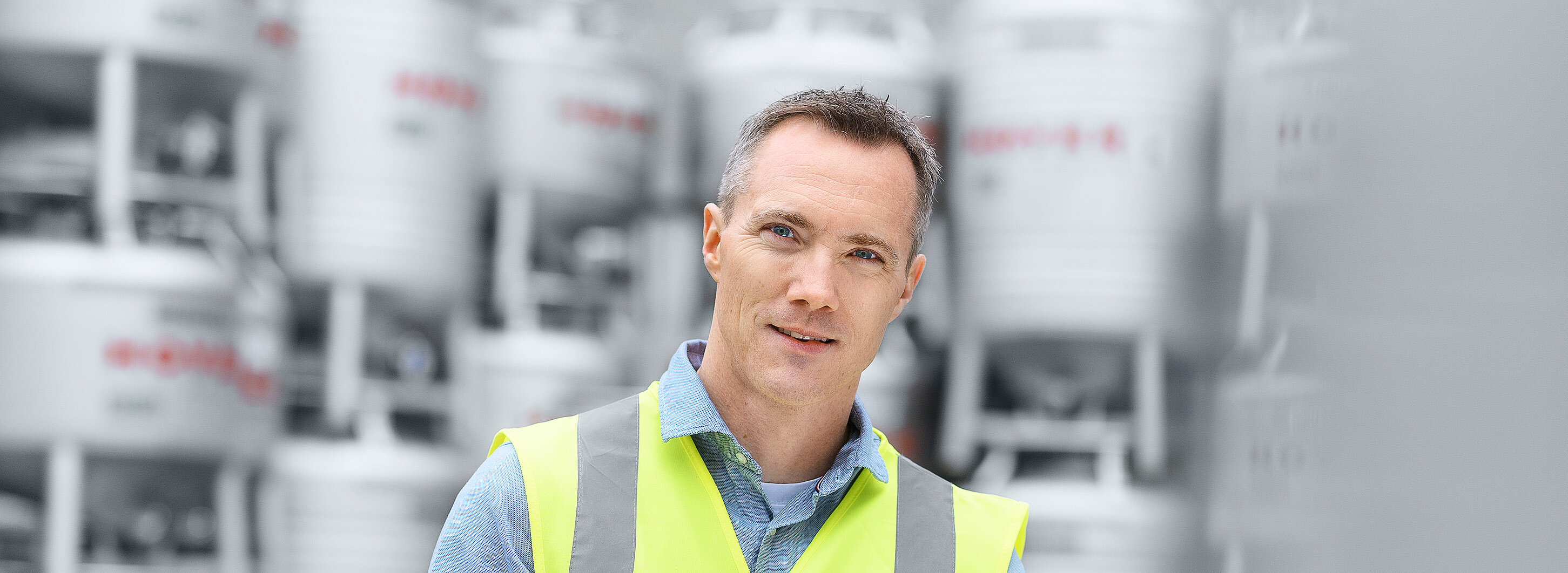 HOYER employee ibc container hi vis vest tablet Employee with safety vest and tablet stands in front of stacked HOYER IBCs in the outdoor areaEmployee with safety vest and tablet stands in front of stacked HOYER IBCs in the outdoor area