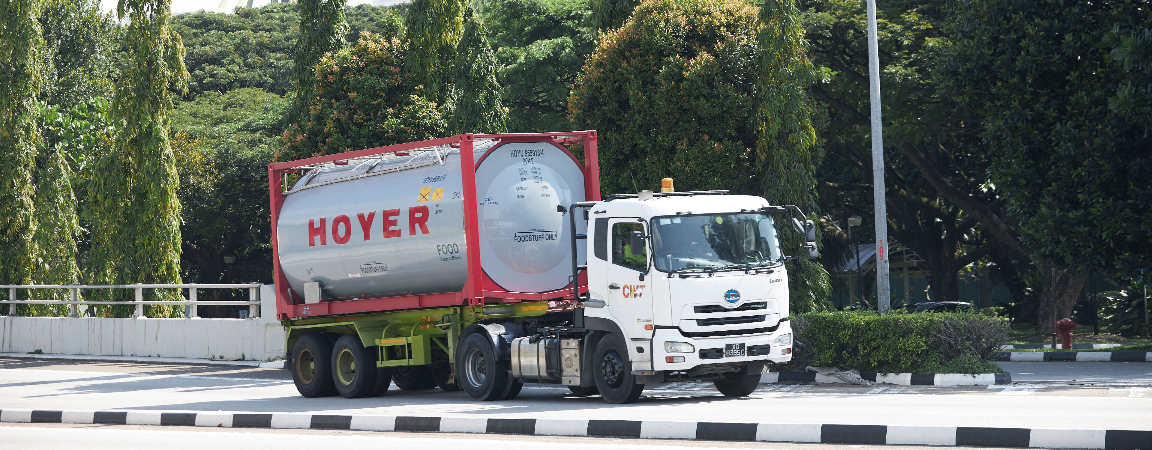 HOYER 食品 罐箱 货车 运输 HOYER 食品罐式集装箱装载于白色卡车(红色框架),在蓝天下经过树木和工业设施