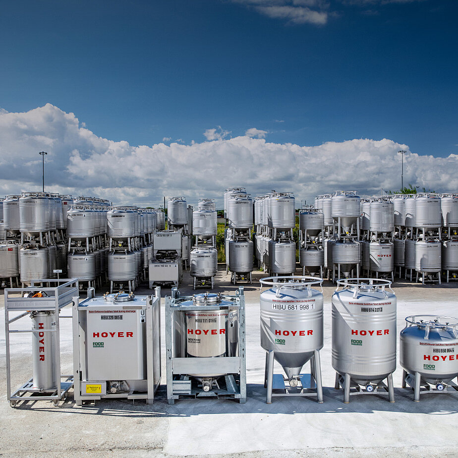 户外储存场地，摆放着多种规格的 HOYER IBC ，并堆放在金属货架上，天空部分多云