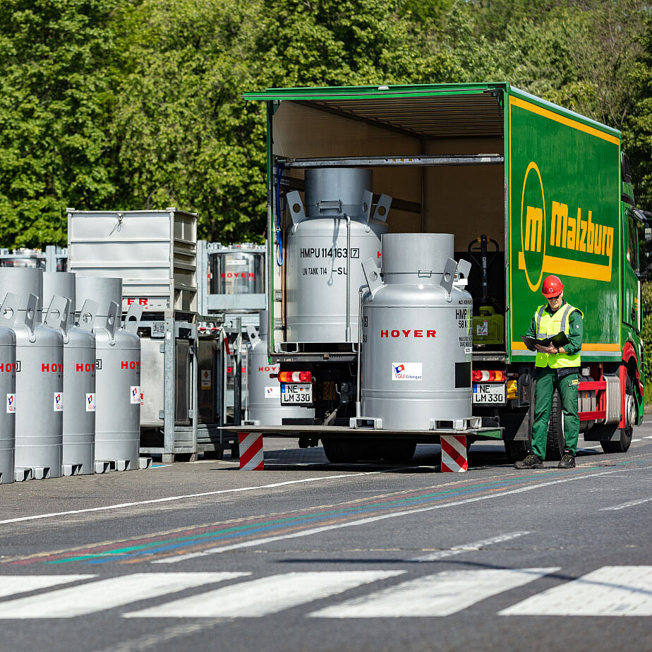 工作人员戴红色安全帽、绿色背心，在户外检查 HOYER IBC 容器装载进绿色卡车的情况