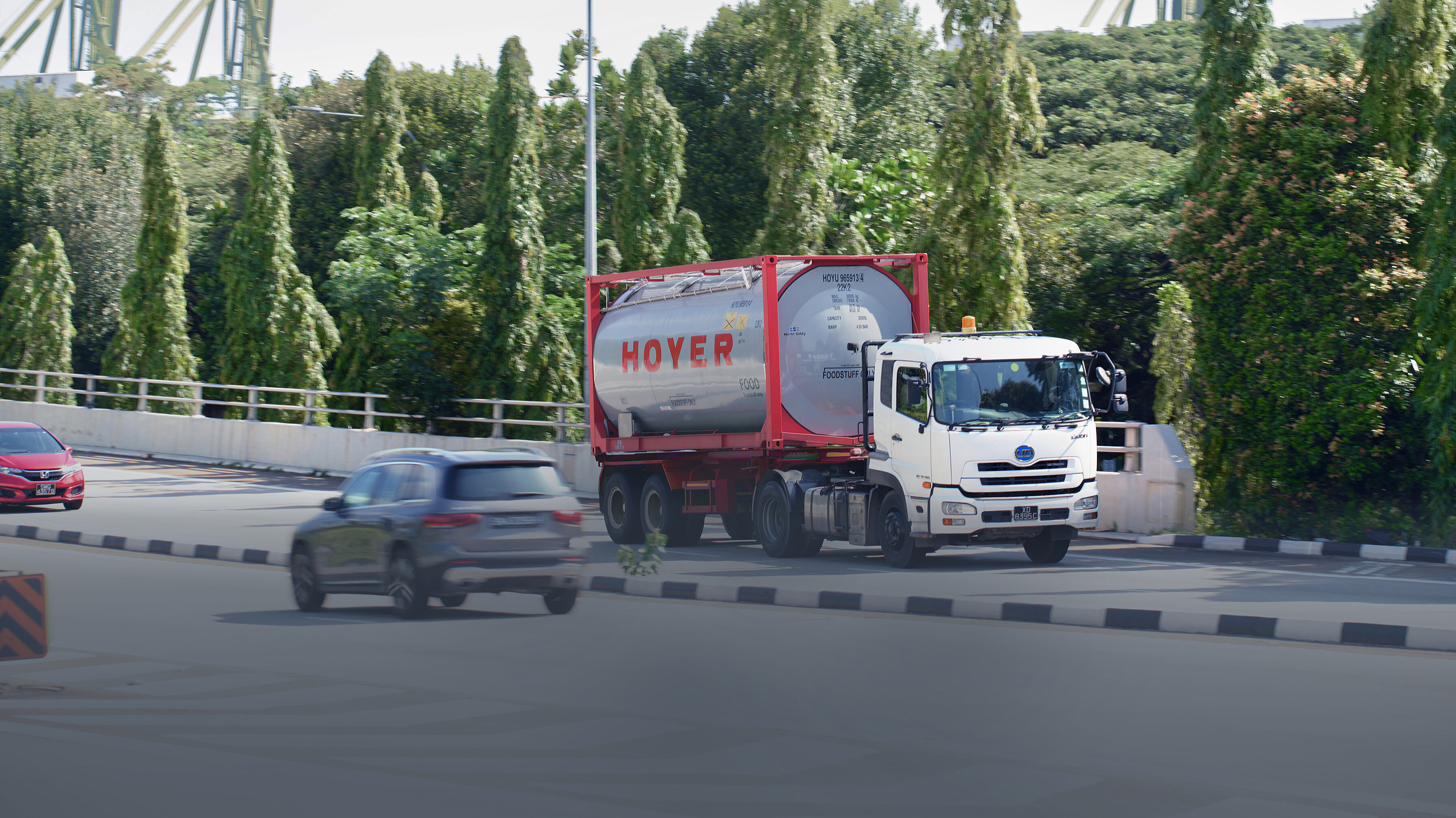 hoyer truck tank container street transport food A white truck with a HOYER food tank container drives on a road surrounded by trees, two cars in the background