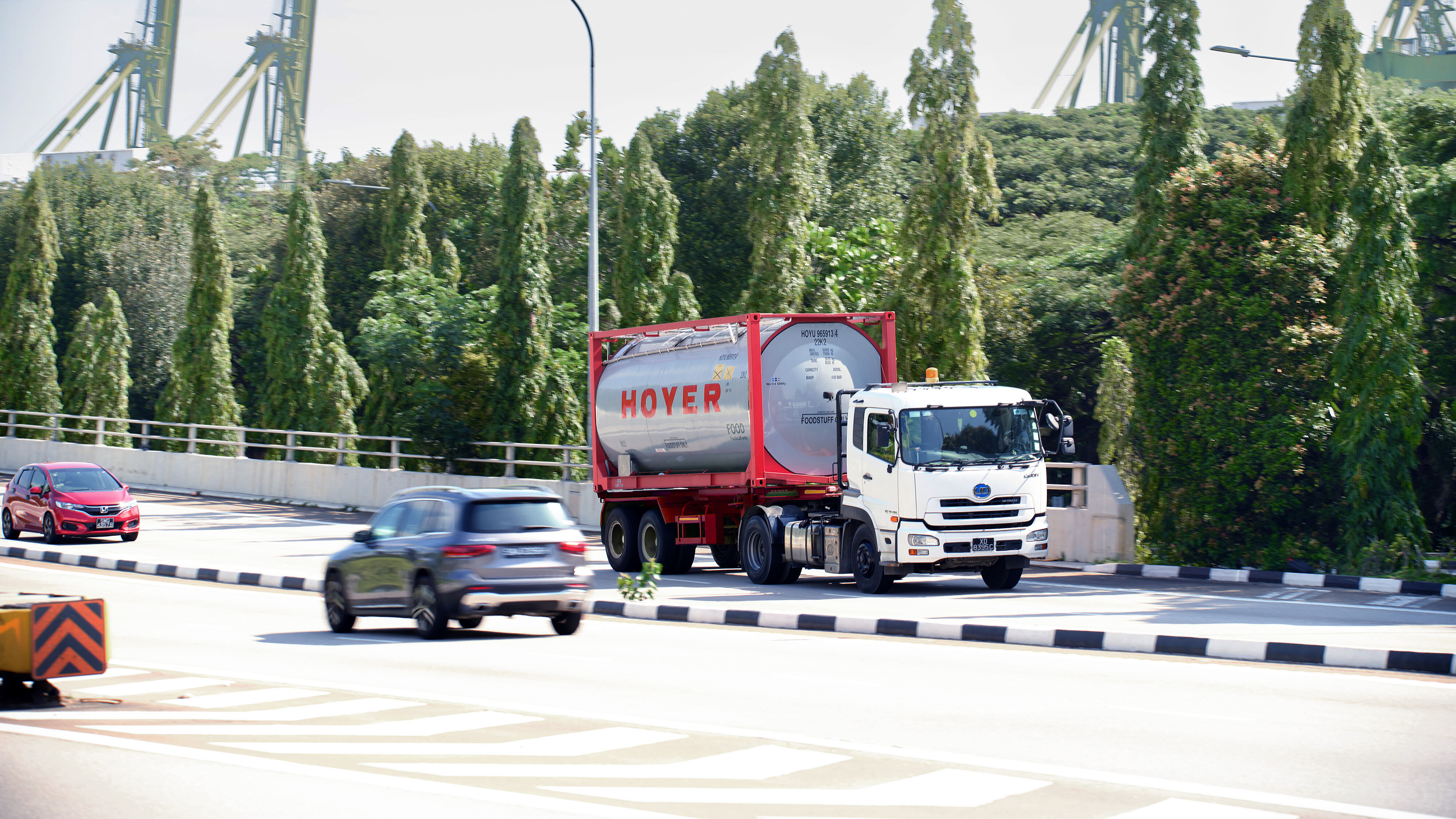 HOYER truck tank container street transport food A white truck with a HOYER food tank container drives on a road surrounded by trees, two cars in the background