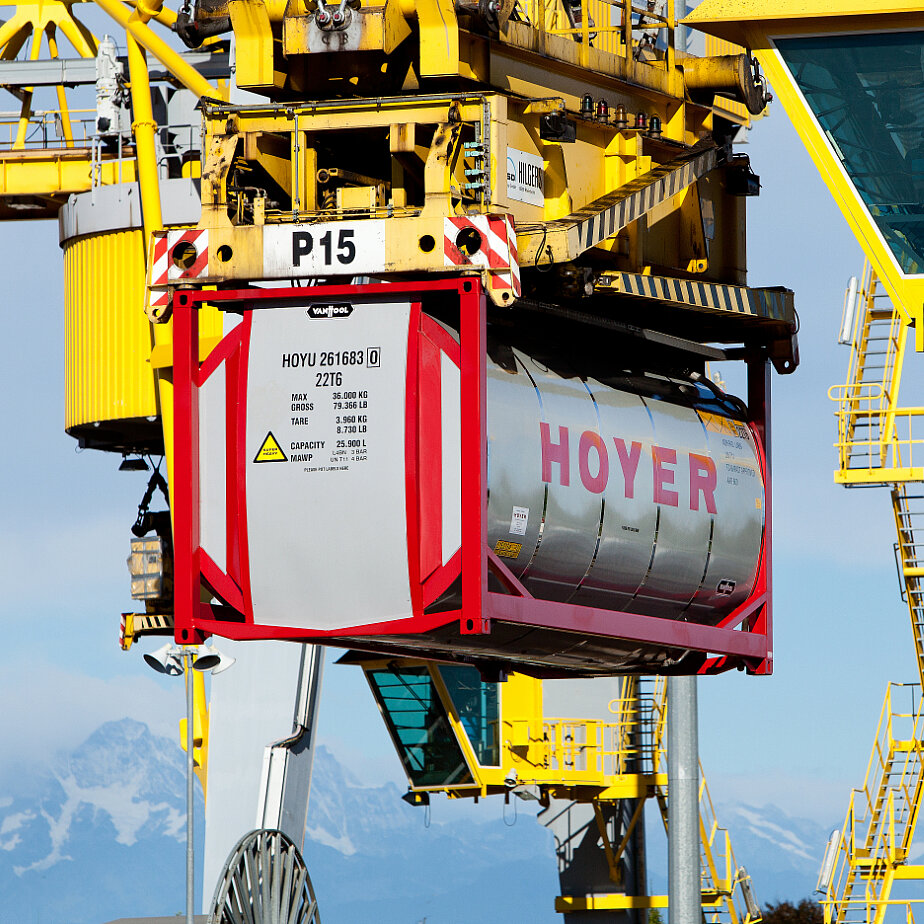 HOYER 化学罐式集装箱由黄色起重机吊起，背景为编号及山地景观