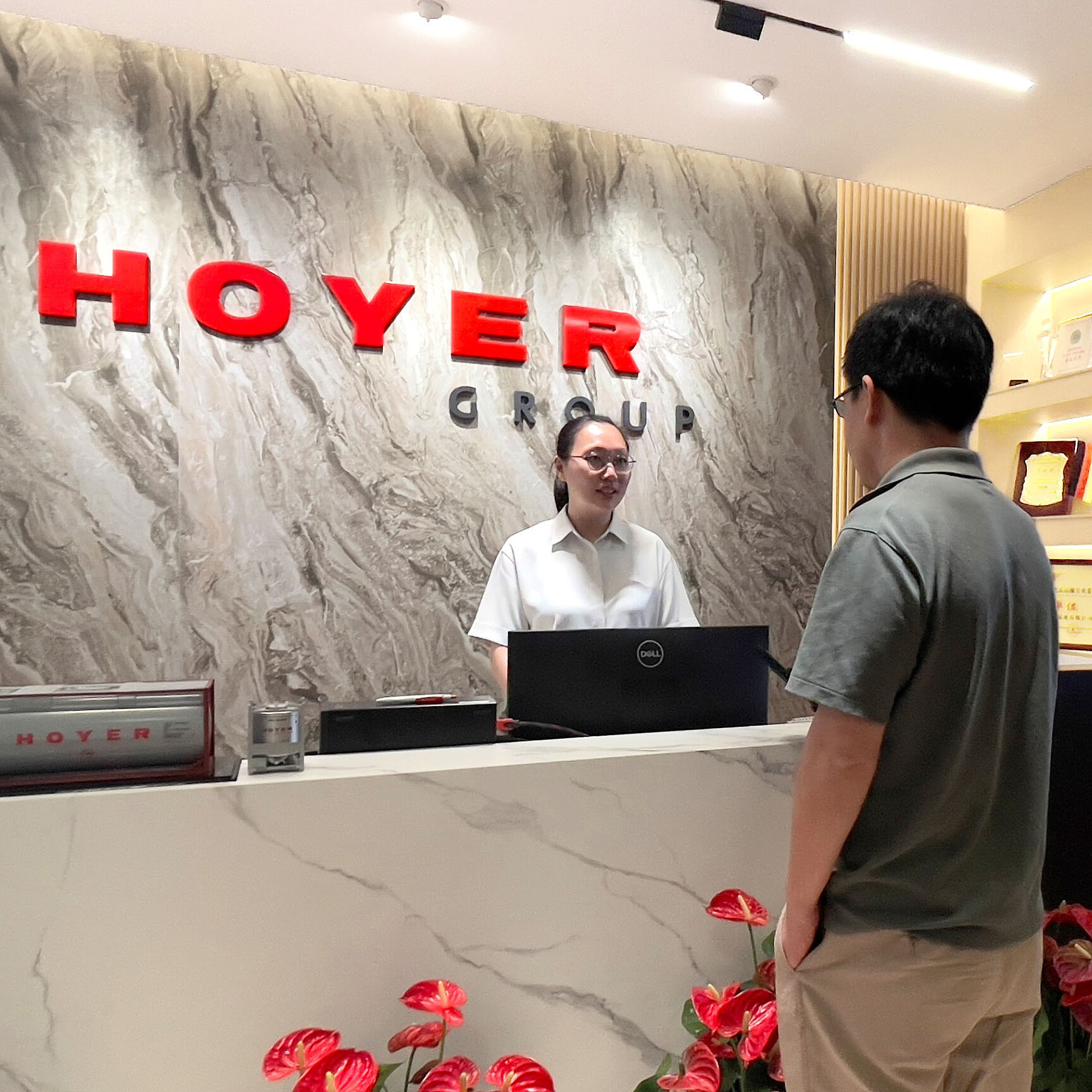 HOYER 集团中国办公区接待大厅，现代化的门厅设有品牌标识、大理石前台、红色鲜花和奖项展示