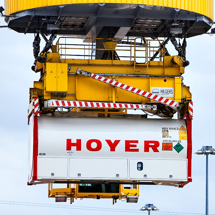 HOYER 气体 罐箱 起重机 危险 标签 光点 HOYER 气体容器贴有危险品标签,正在物流终端被黄色起重机吊装,起重机带红白安全条纹