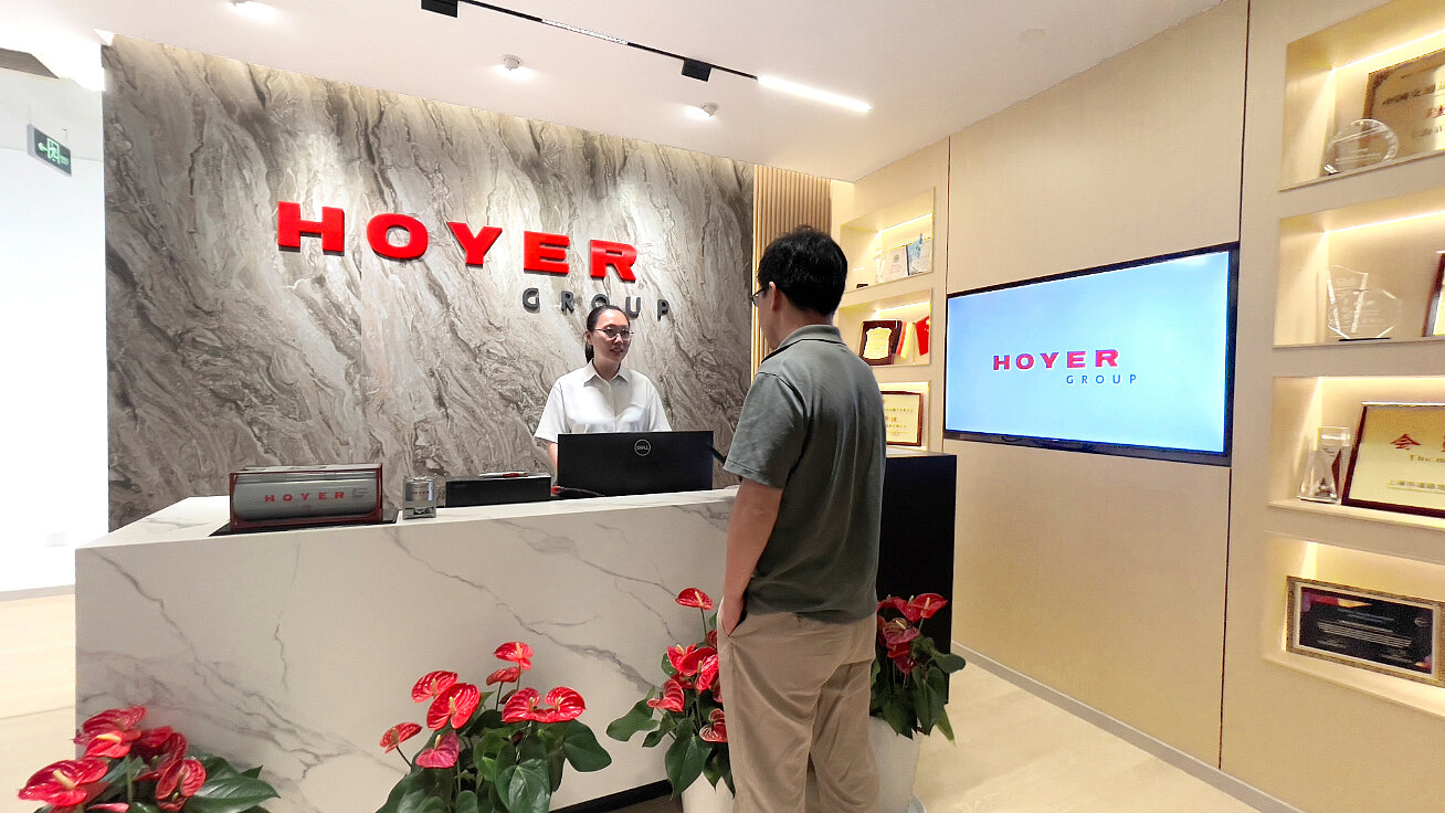 HOYER 集团中国办公区接待大厅，现代化的门厅设有品牌标识、大理石前台、红色鲜花和奖项展示