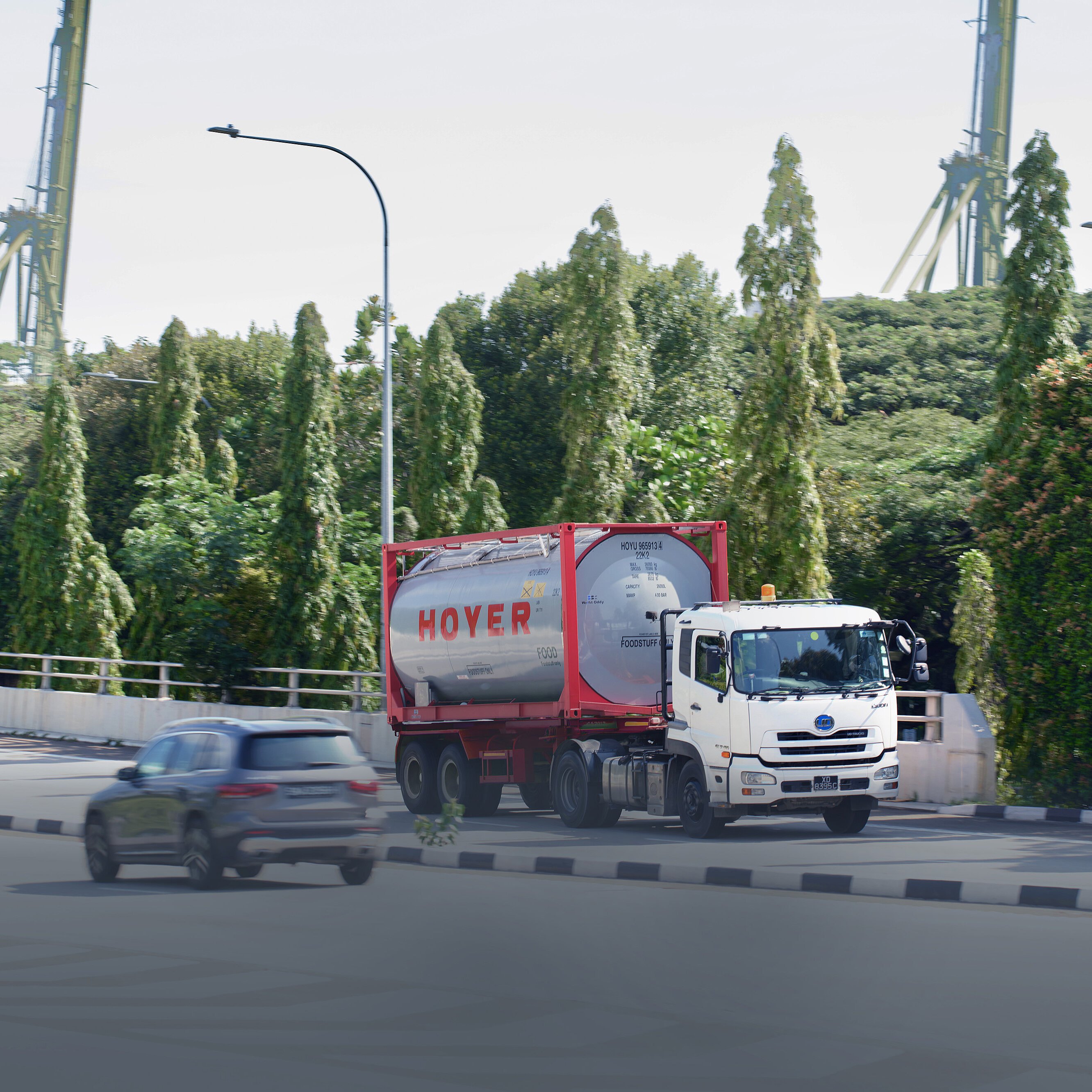 hoyer truck tank container street transport food A white truck with a HOYER food tank container drives on a road surrounded by trees, two cars in the background