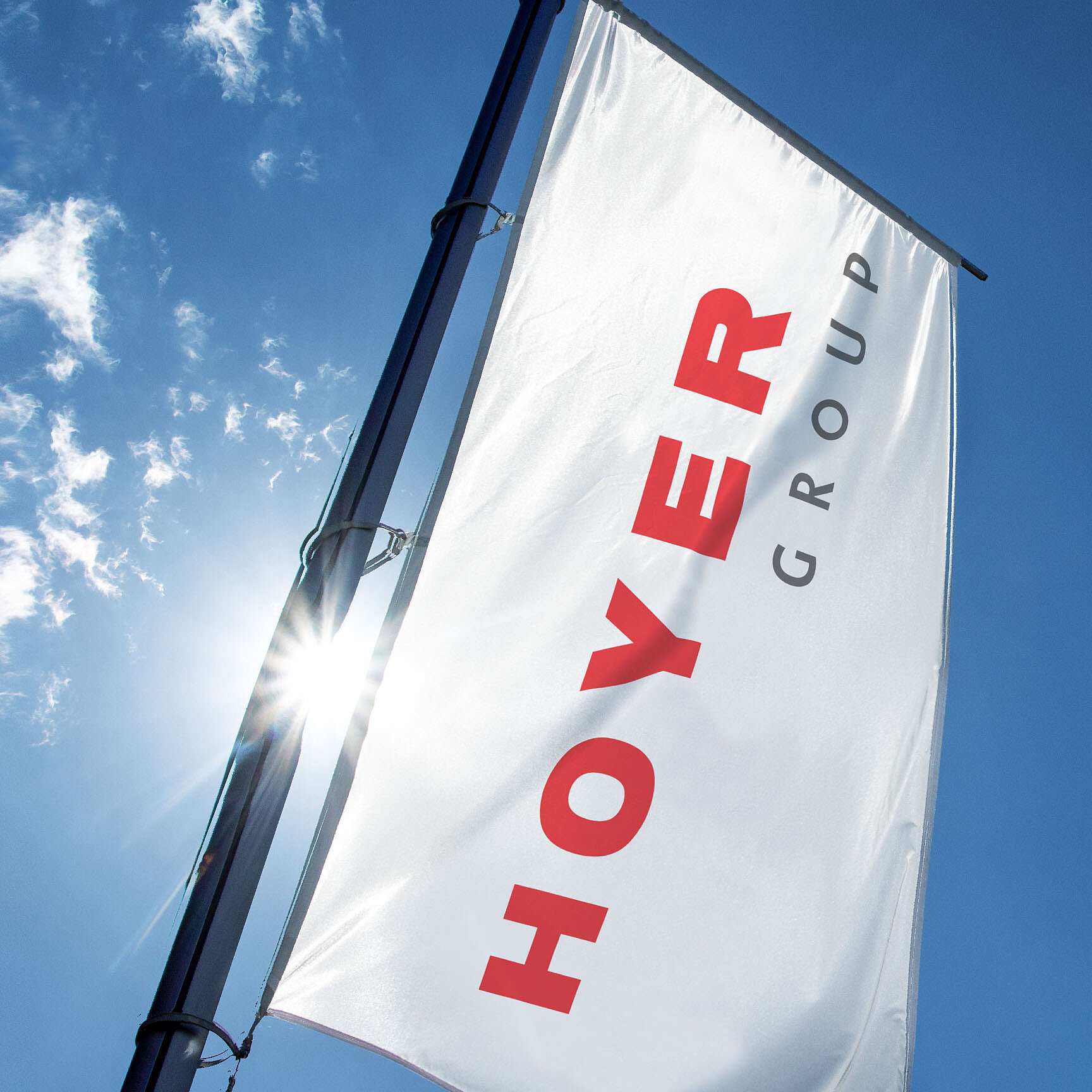 印有红黑字样的 HOYER 集团公司旗帜在蓝天白云与阳光下迎风飘扬