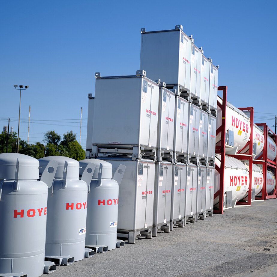 HOYER IBC 容器 堆场 户外仓储区堆放的 IBC 容器和 HOYER 罐式集装箱,背景有树木、电线及蓝天