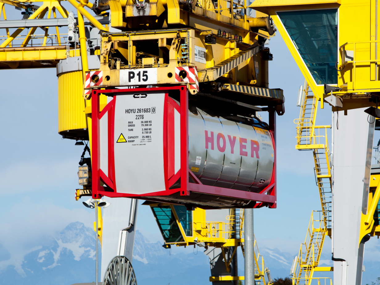 HOYER 化学罐式集装箱由黄色起重机吊起，背景为编号及山地景观