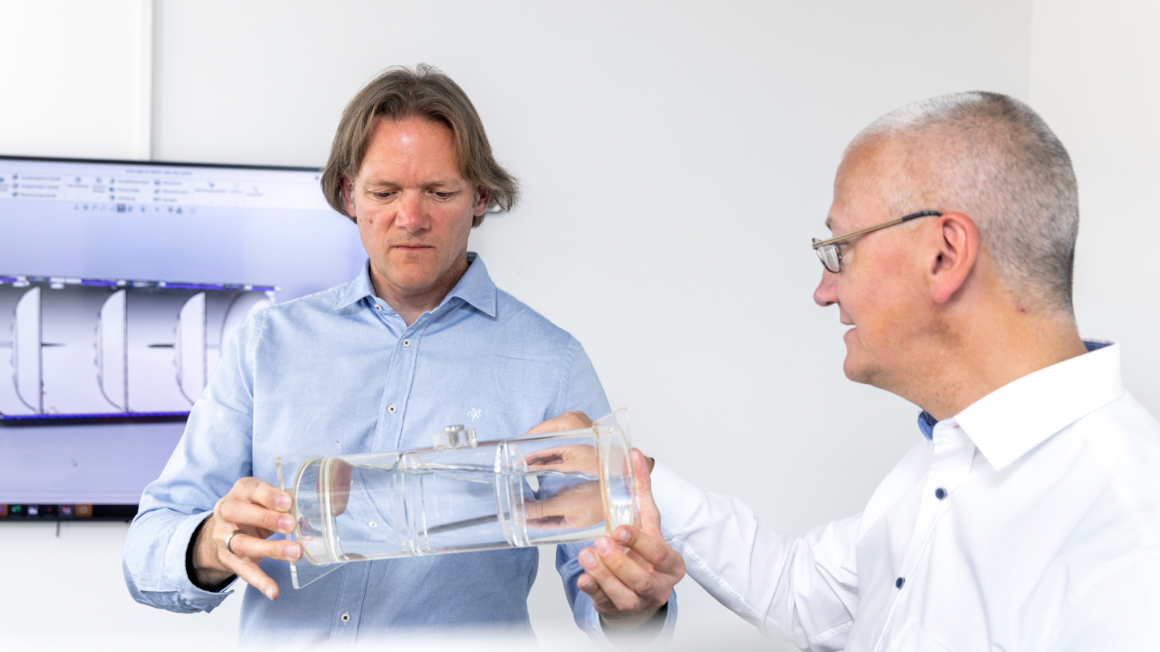 Two engineering colleagues discussing a transparent model used to demonstrate the effect of baffle walls in tank containers