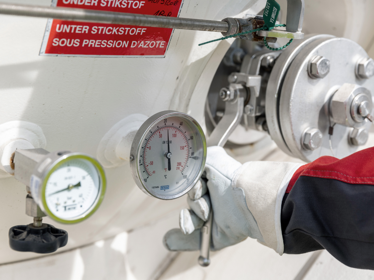 氮气系统气体接口及压力表特写，戴手套的手使用扳手调整阀门