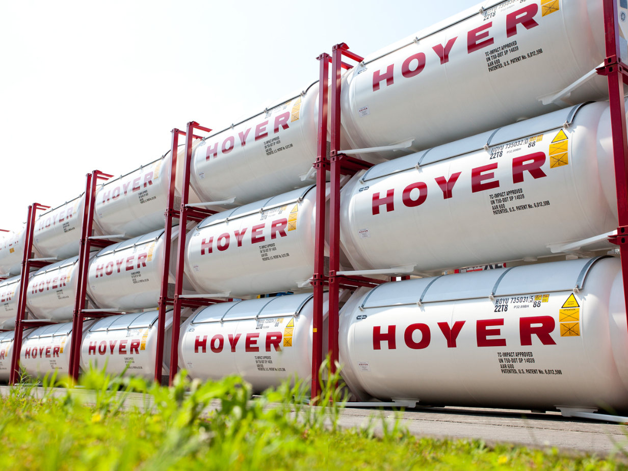 Stacked HOYER gas tank containers with red frames and safety labels, organized depot site