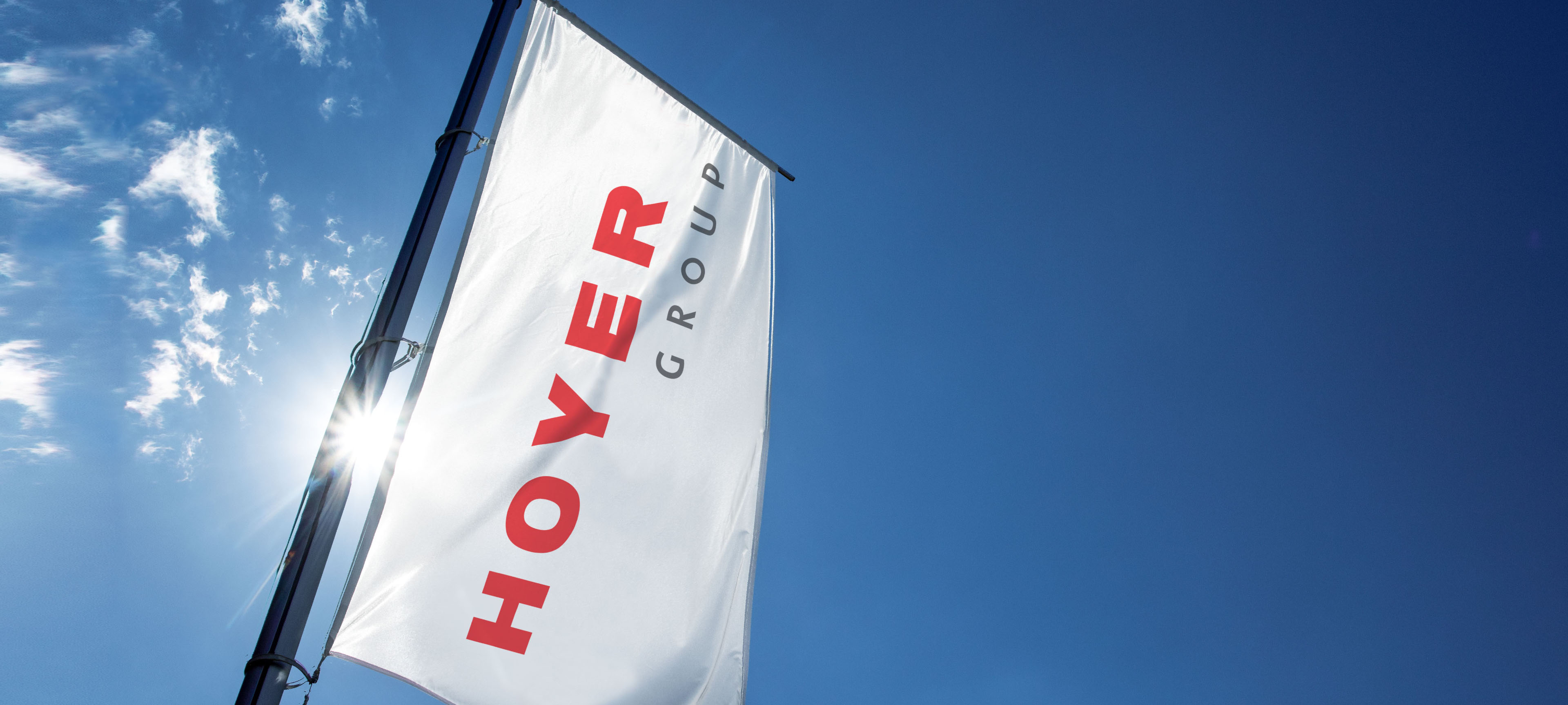 印有红黑字样的 HOYER 集团公司旗帜在蓝天白云与阳光下迎风飘扬