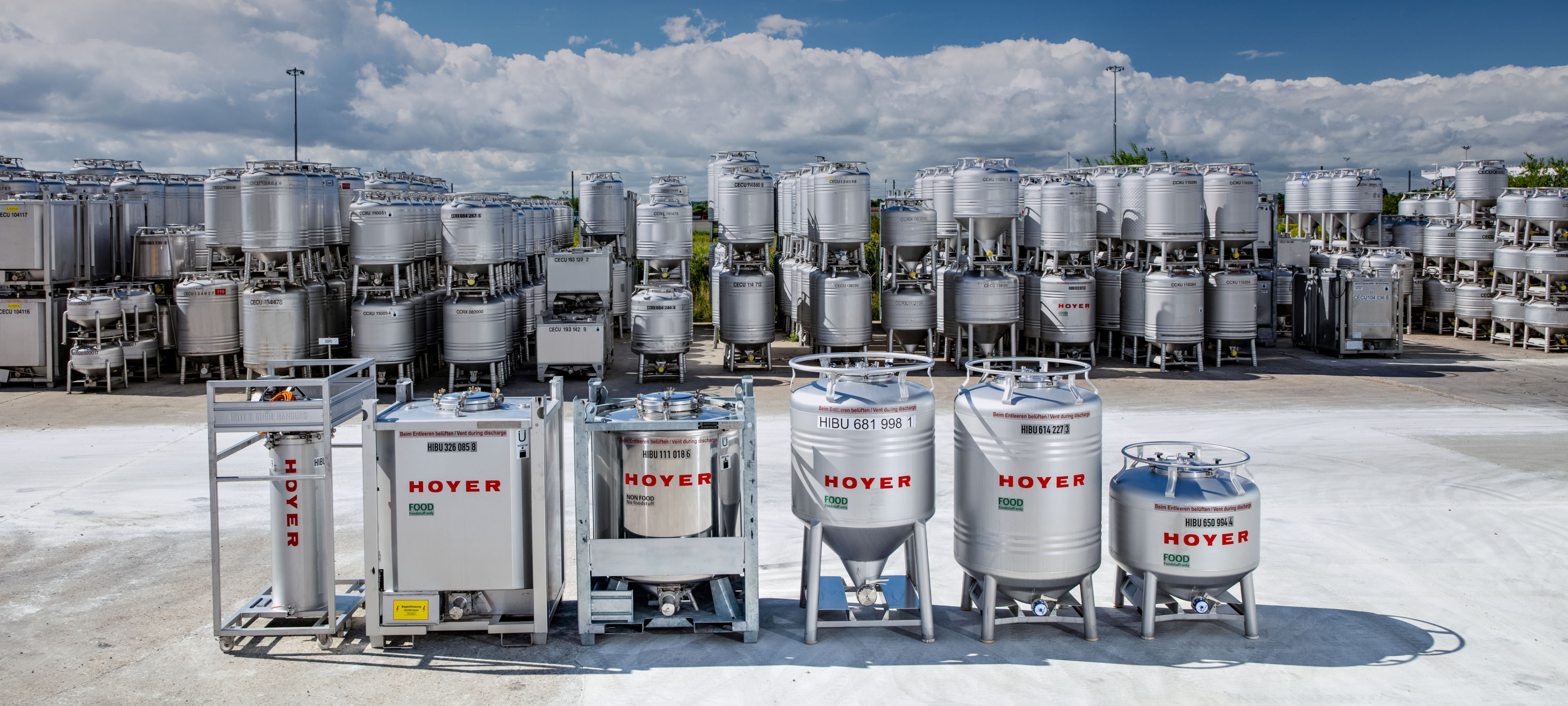 户外储存场地，摆放着多种规格的 HOYER IBC ，并堆放在金属货架上，天空部分多云